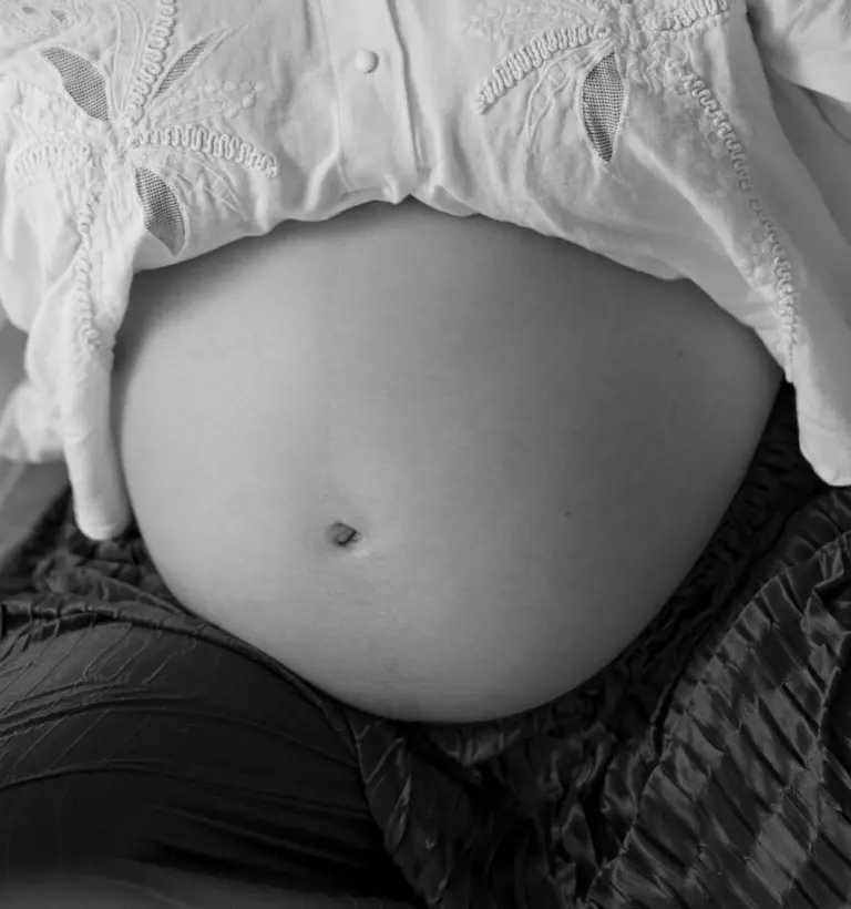 Détail en noir et blanc d'un ventre rond sous une chemise brodée